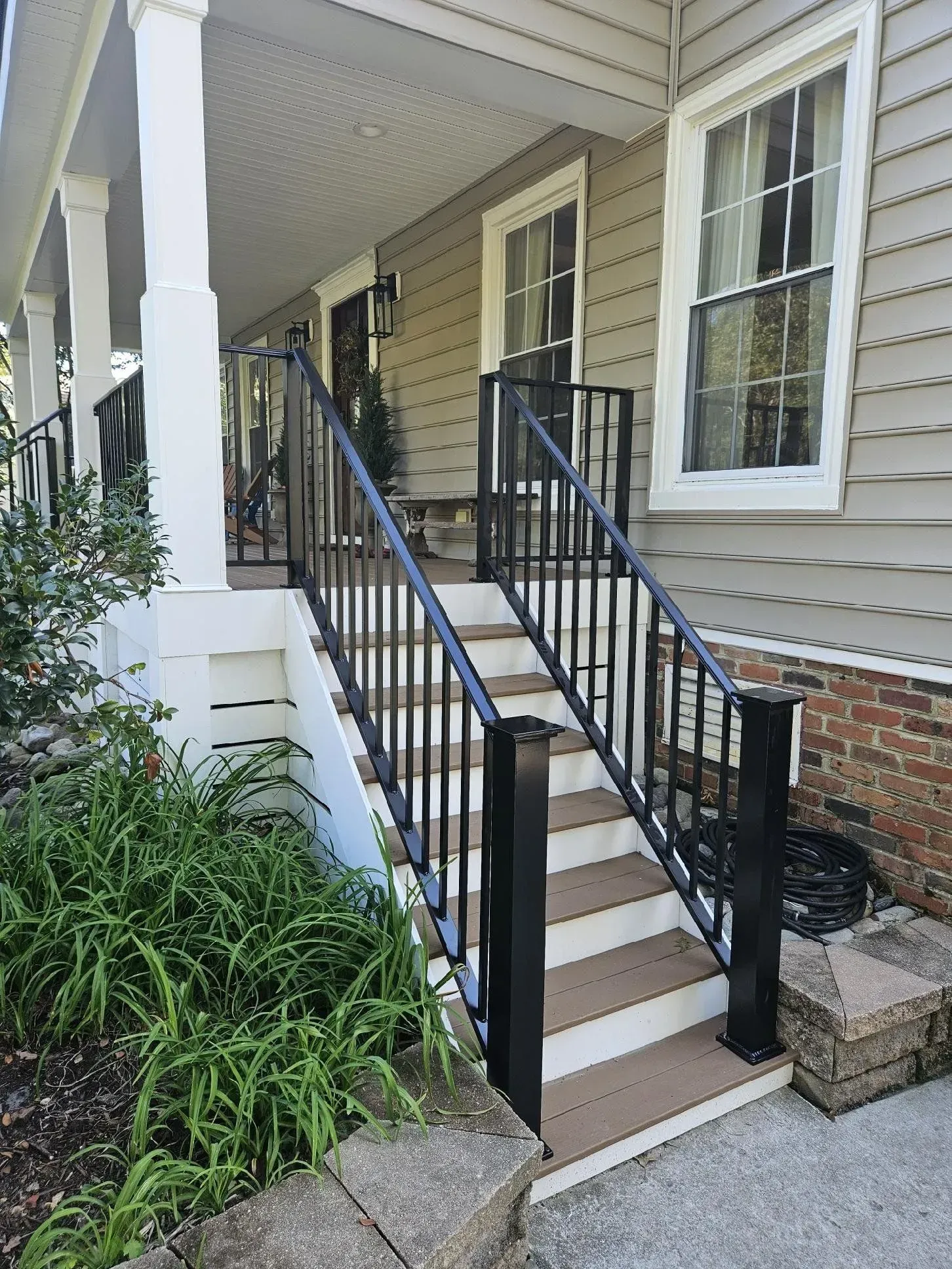A black wrought-iron railing flanks outdoor stairs leading to a home's porch.
