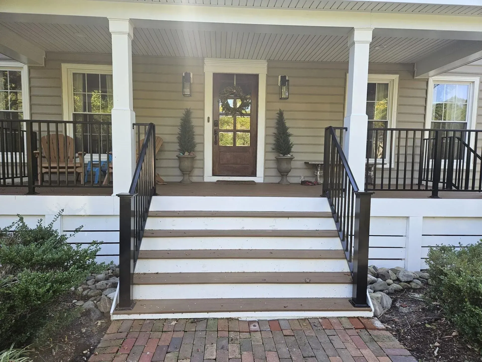 A home's front porch with a brick walkway and steps. Black railings and white columns frame the entrance.