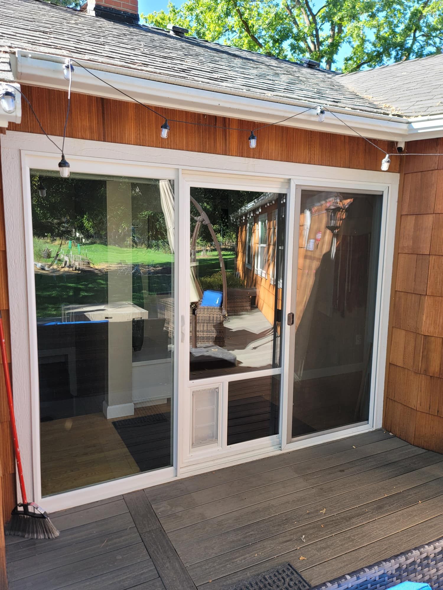 Sliding glass door with built-in pet door on a wood deck; string lights overhead.