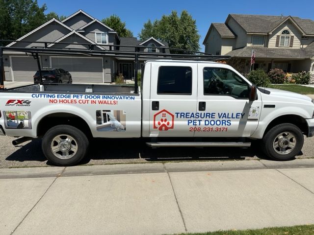 White truck with Treasure Valley Pet Doors logo parked on a sidewalk in front of houses.