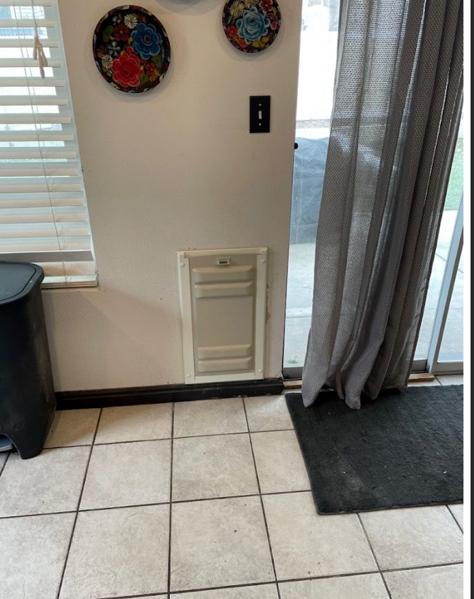 A dog door on a wall beside a sliding glass door and a window. Two decorative plates hang above.