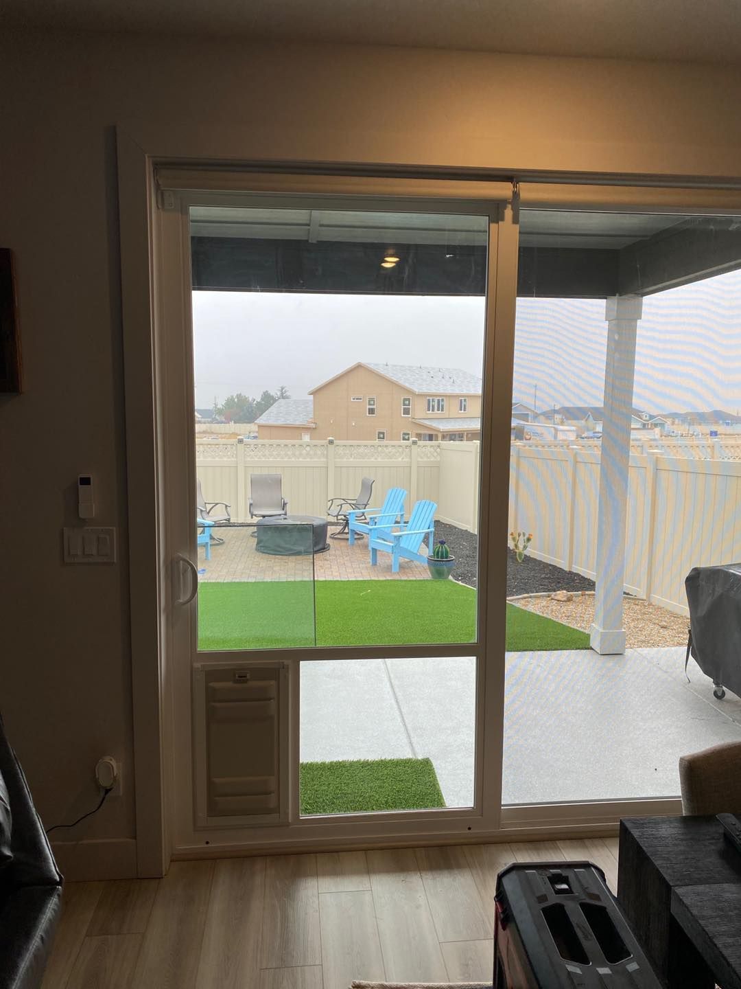 Sliding glass door with pet door; view of backyard with furniture, artificial turf, and white fence.