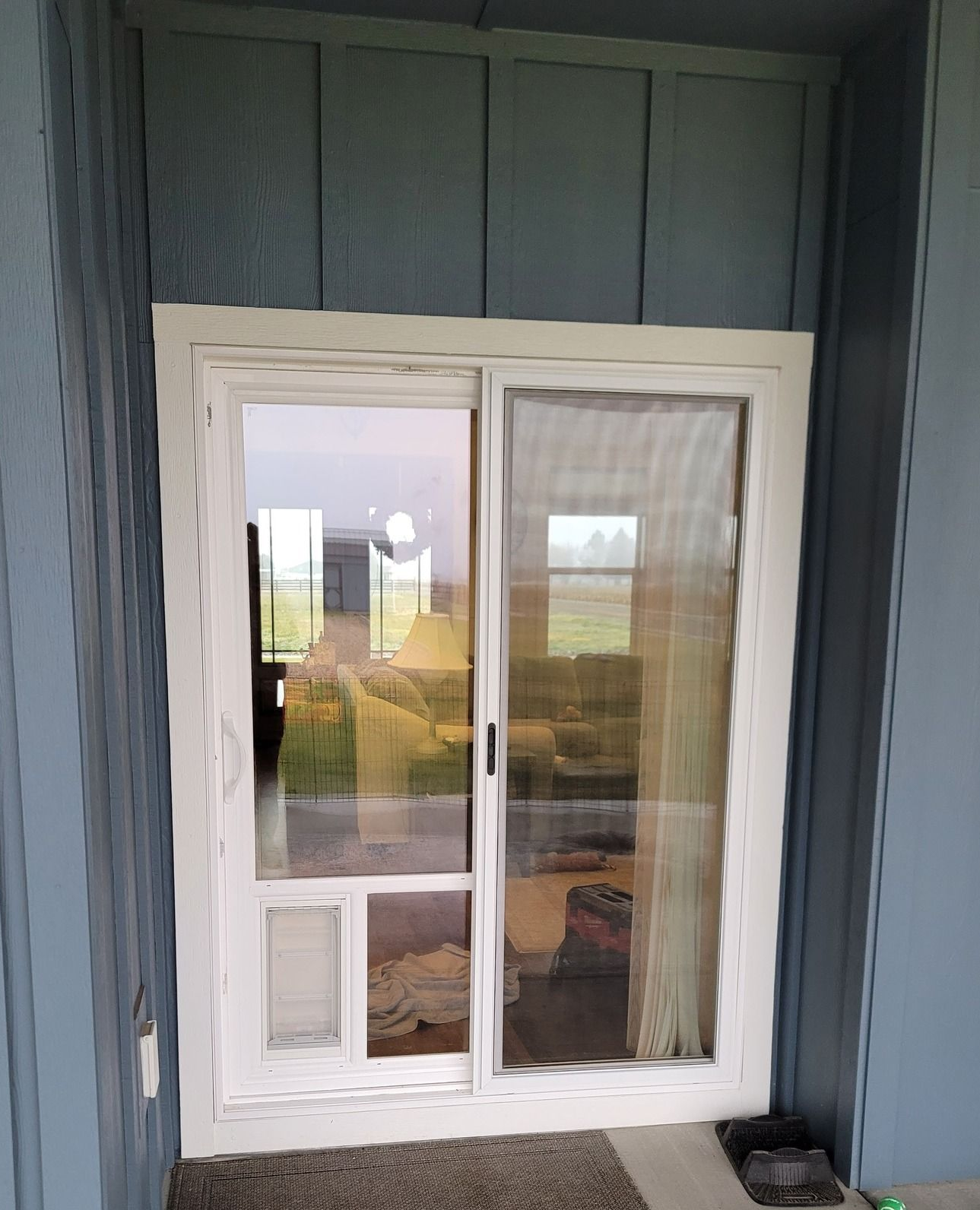 White sliding glass door with a built-in pet door, set in blue siding.