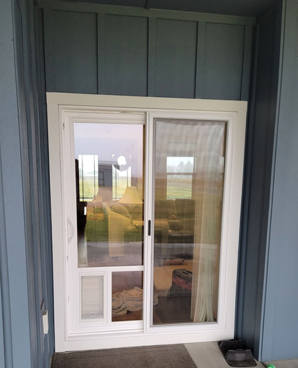 White sliding glass door with a built-in pet door, set in blue siding.