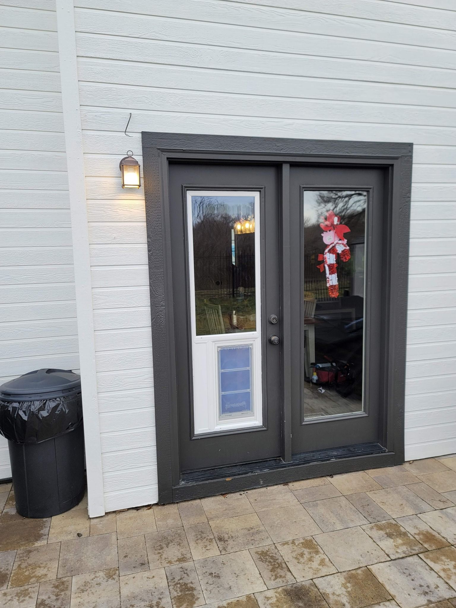 Exterior view of dark gray double doors with dog door, outdoor light, and trash can.