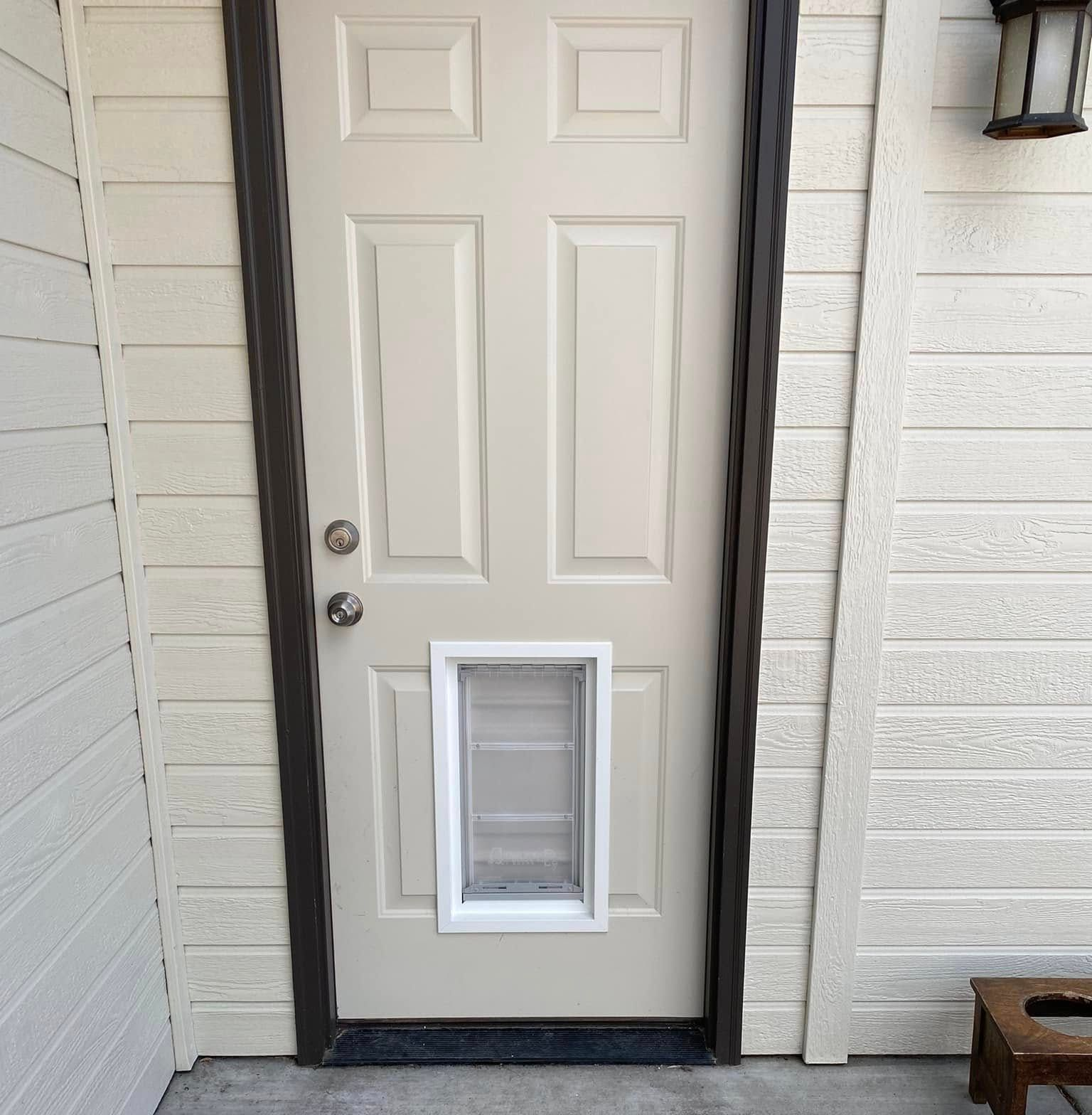 Tan door with a white pet door installed. Door set in a beige wall.
