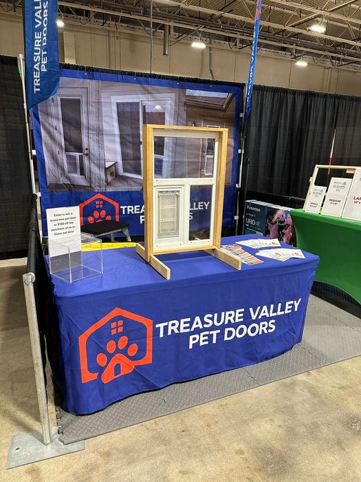 Trade show booth for Treasure Valley Pet Doors, featuring a pet door display. Blue table with logo, window sample.