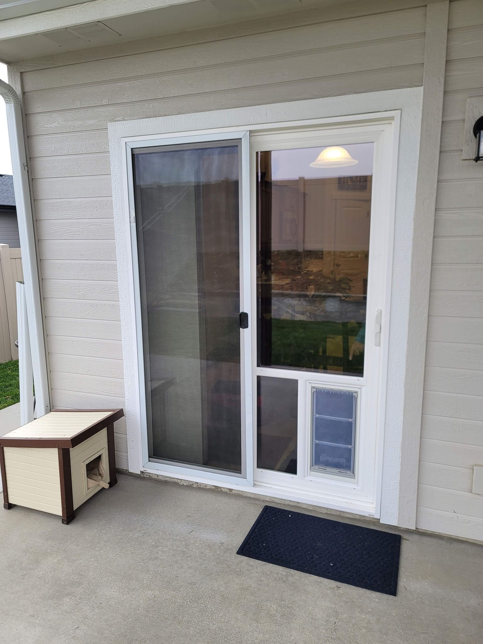 Sliding glass door with built-in pet door and a cat house on a porch.