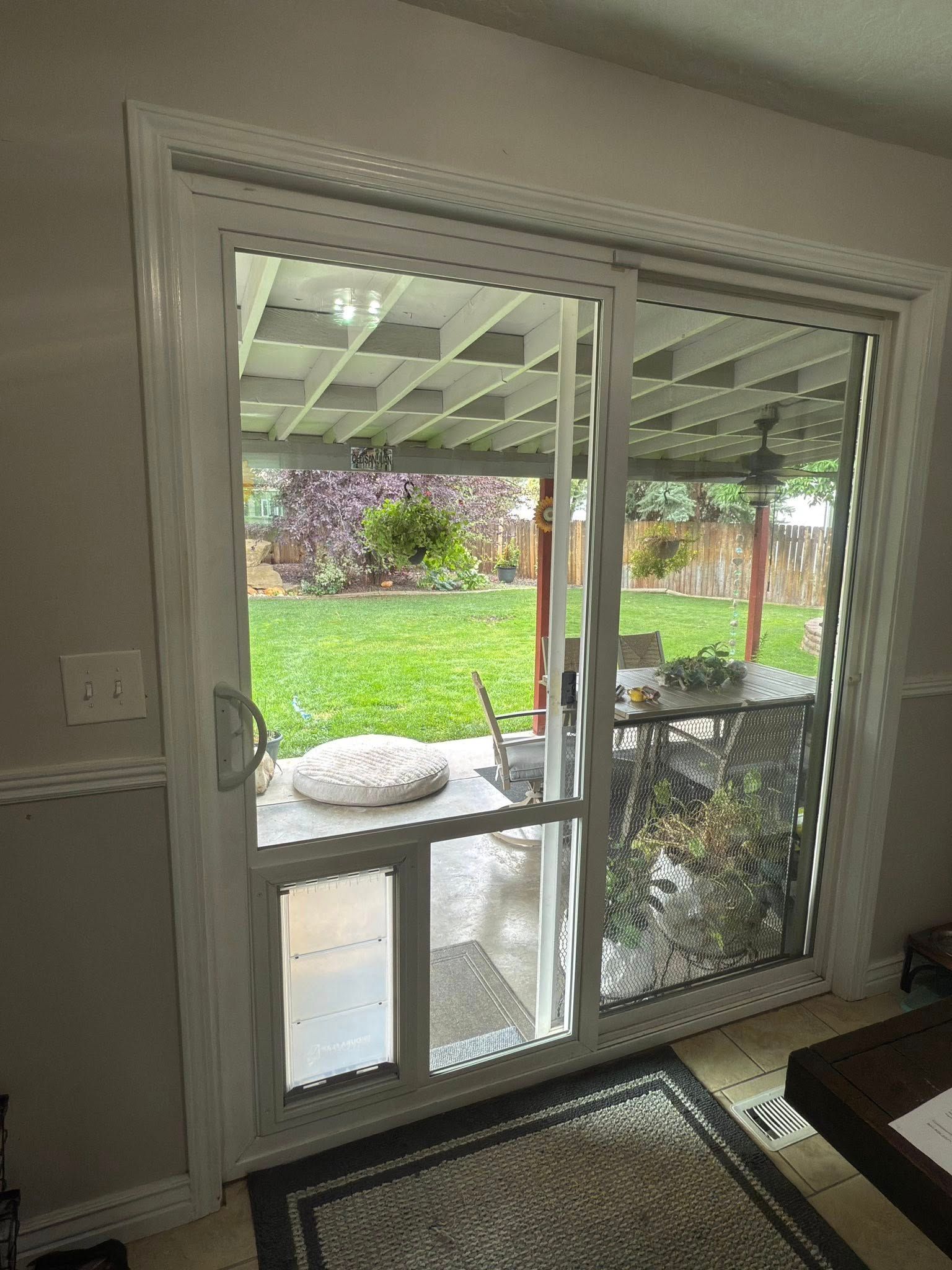 Sliding glass door with built-in pet door opens to a backyard with grass and patio furniture.