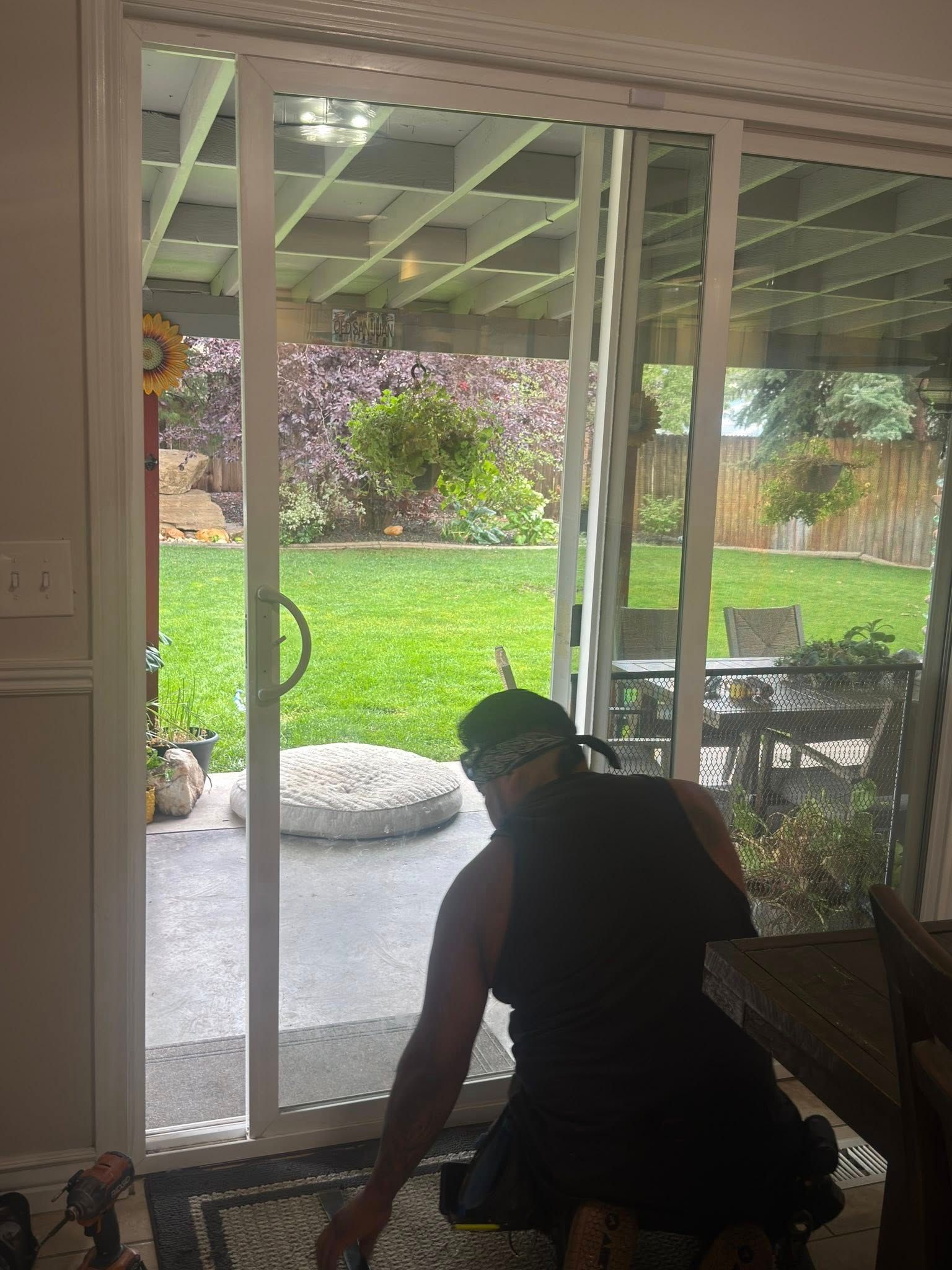 Person working on a sliding glass door. A backyard with greenery is visible through the door.