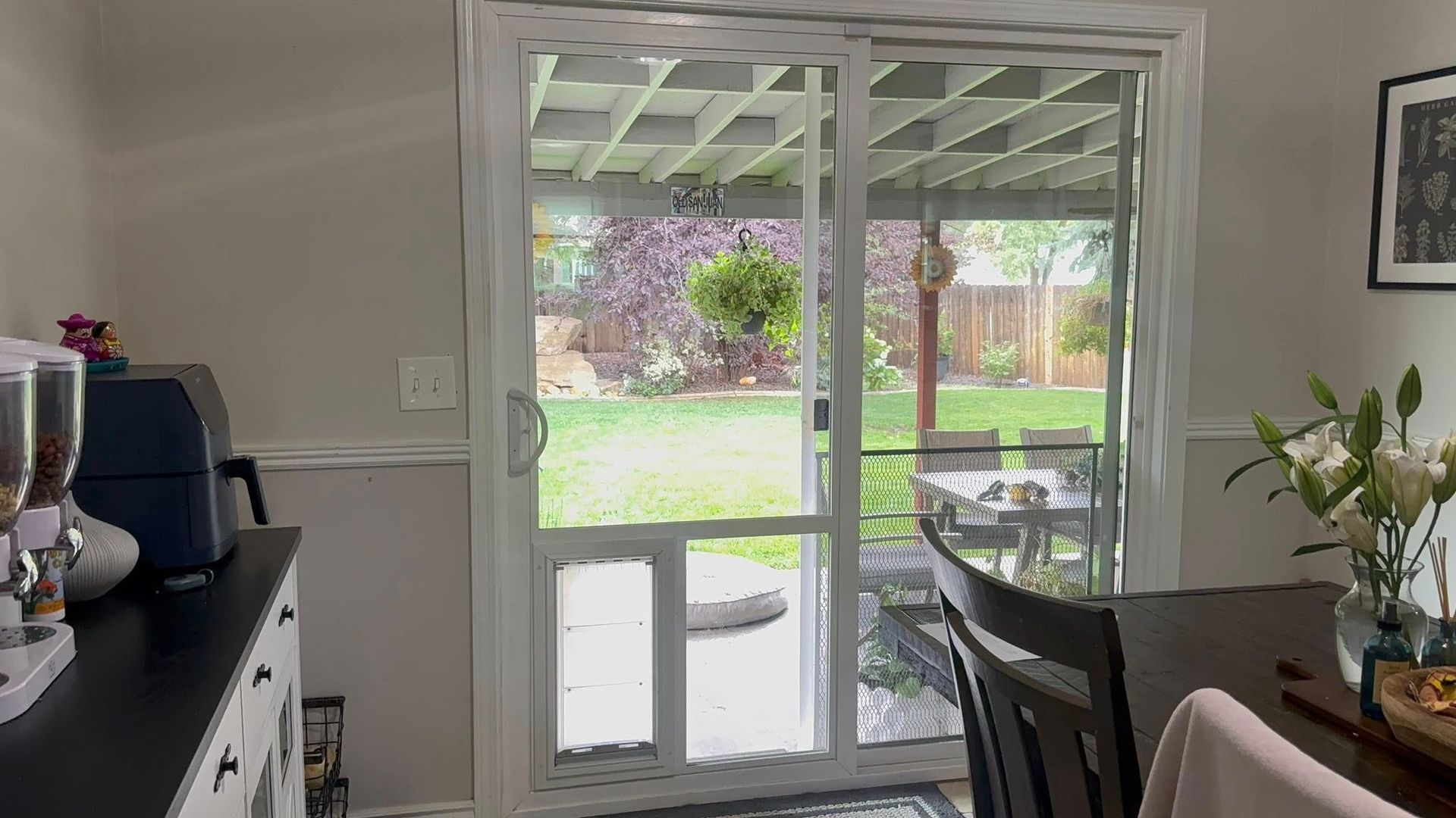Interior view of a room with a sliding glass door open to a backyard with grass and trees.