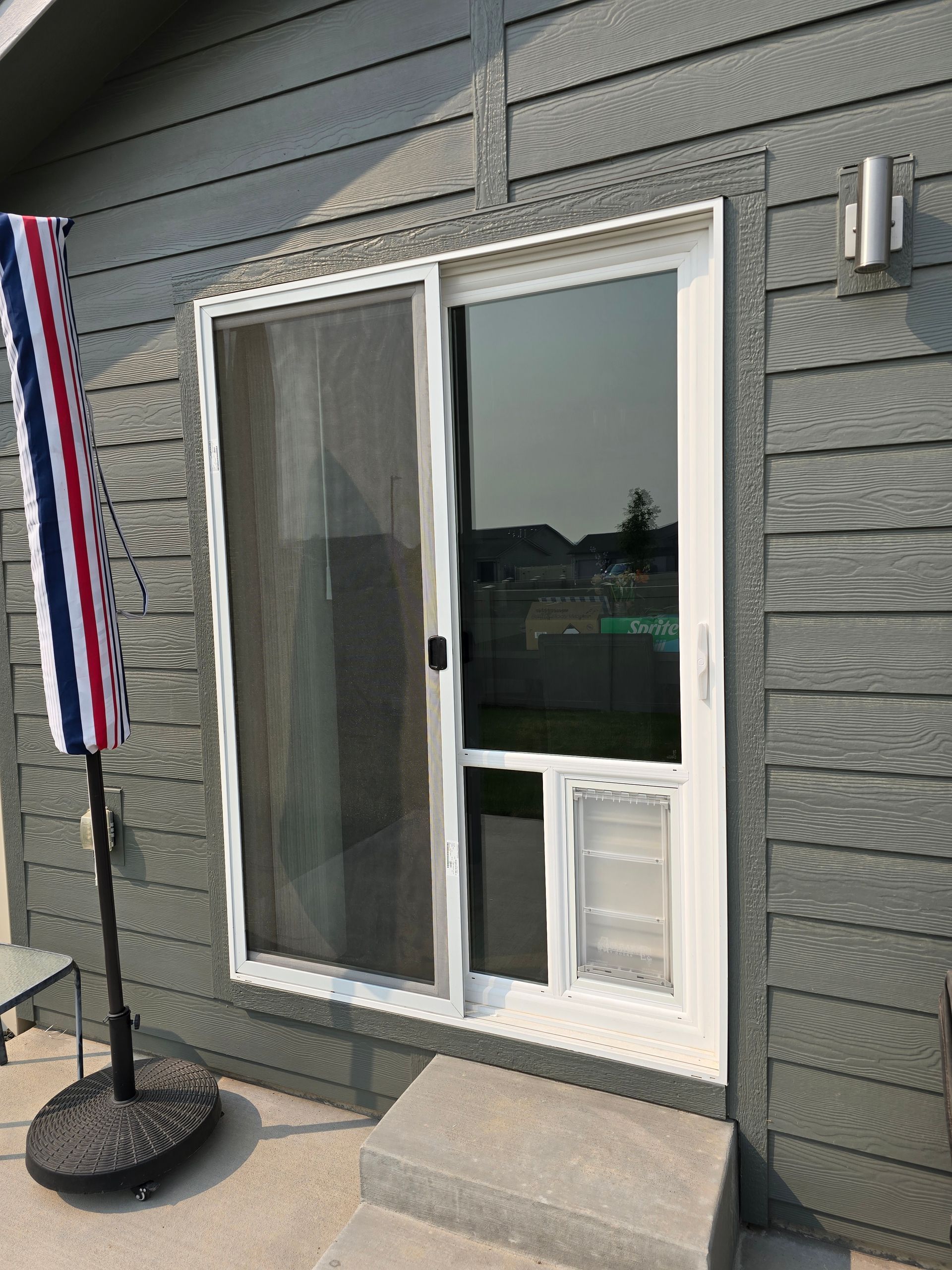 Sliding glass door with built-in pet door; grey siding, patio, and an umbrella to the left.