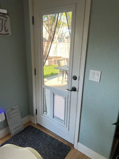 White exterior door with a dog door leading to a patio with a table and chairs and a yard.