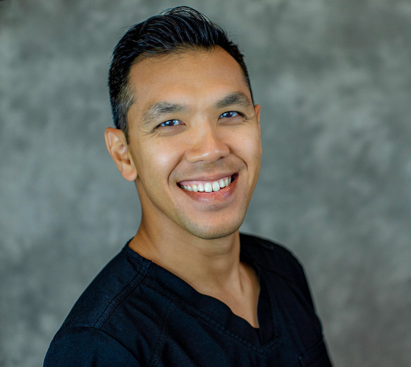 A man in a black scrub top is smiling for the camera.