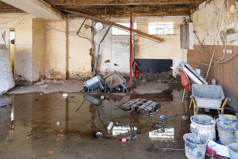 Flooded, cluttered basement with debris, buckets, and water on the floor after damage.