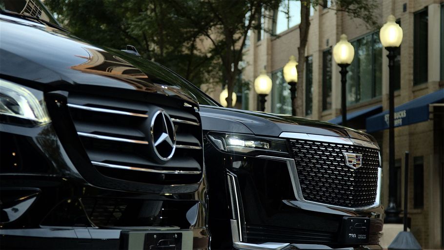 Close-up of two black Mercedes vehicles parked on a city street at night, with lit streetlamps and buildings behind.