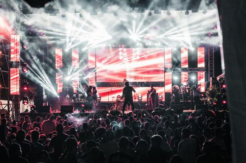 Concert crowd facing bright red stage lights and LED screens at a live music event