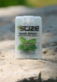 A bottle of suze mask spray is sitting on a rock.