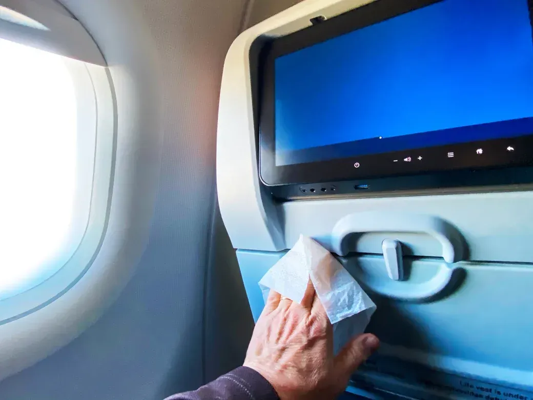 A person is cleaning an airplane monitor with a napkin