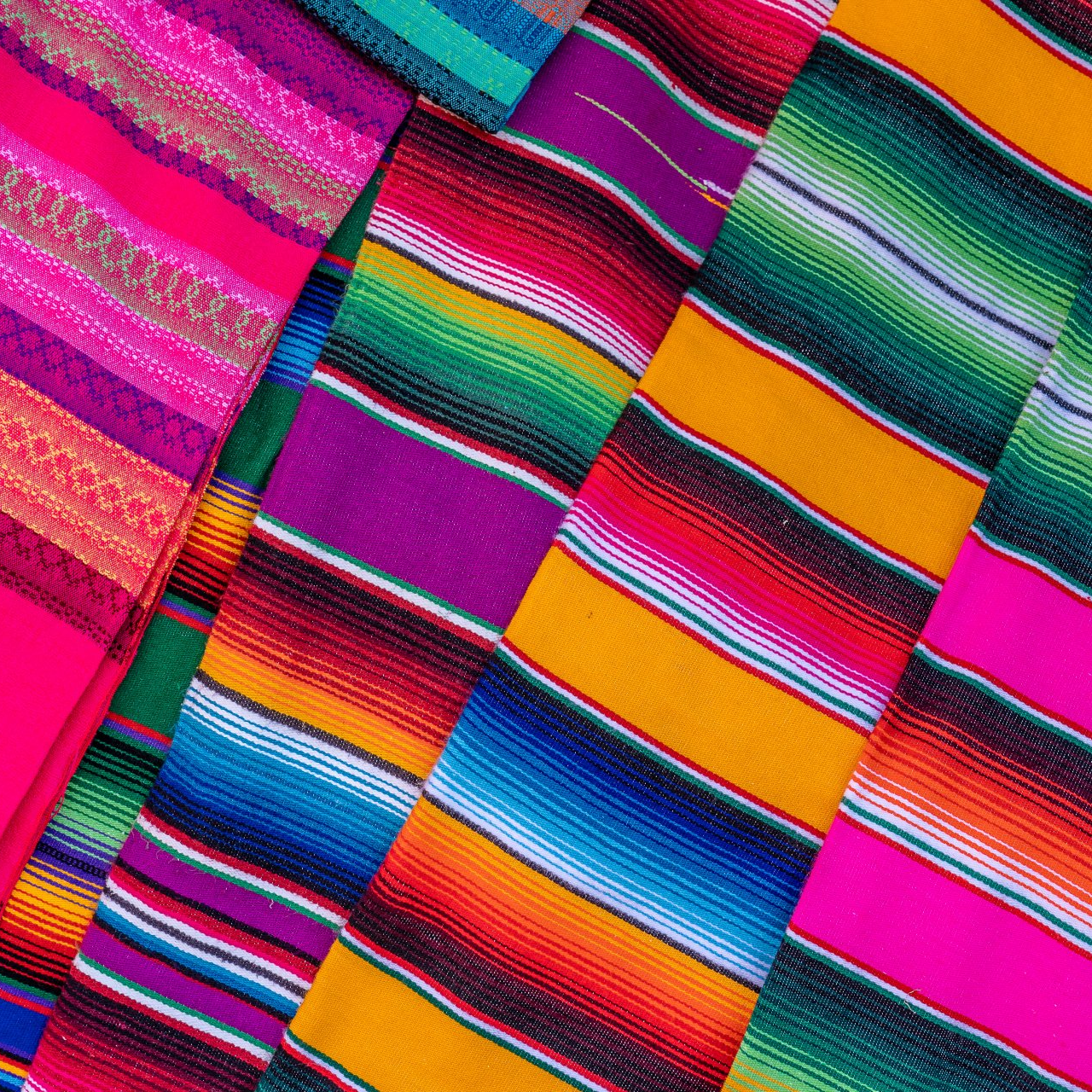 A bunch of colorful blankets are stacked on top of each other.