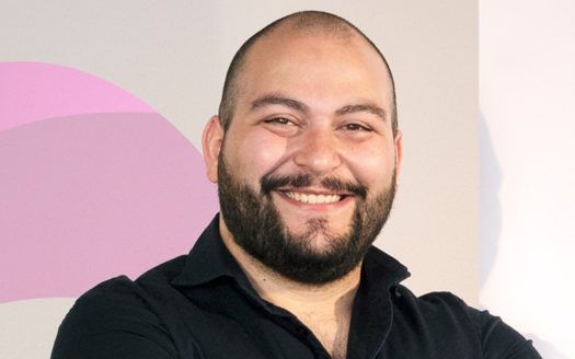 Un homme chauve avec une barbe sourit à la caméra.