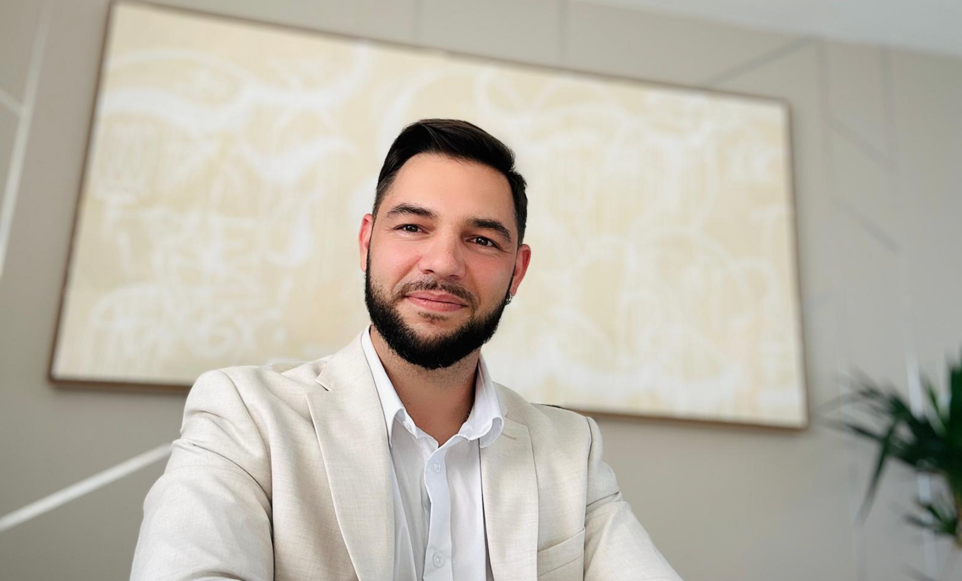 Un homme avec une barbe est assis à un bureau devant un tableau.