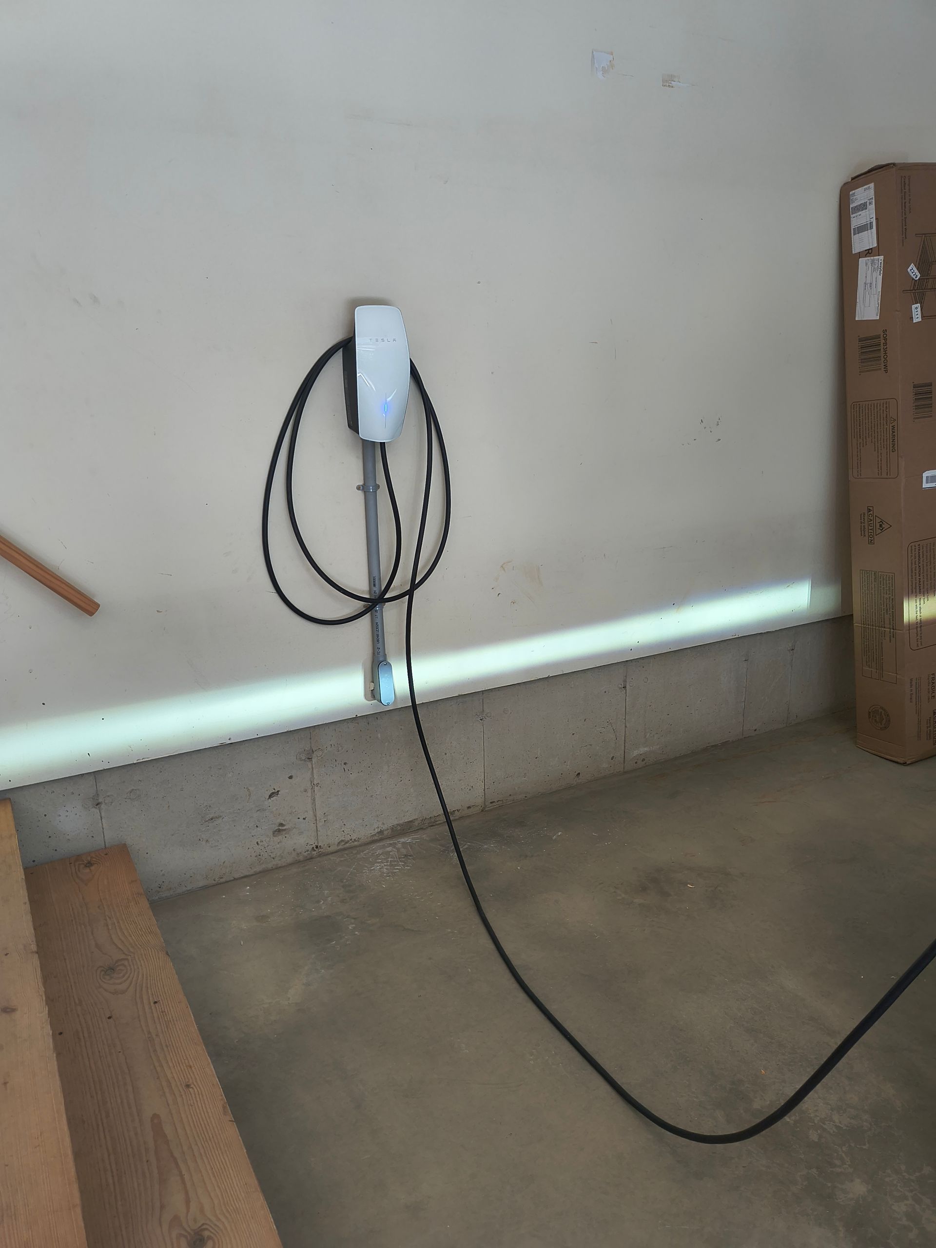 Electric vehicle charger mounted on a garage wall, with coiled cable and concrete floor.