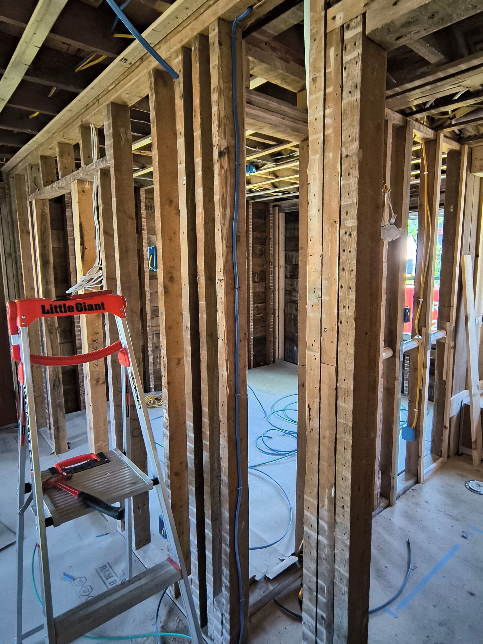 Interior construction: bare wooden studs and framing. A ladder leans against the wall, wires run along the structure.