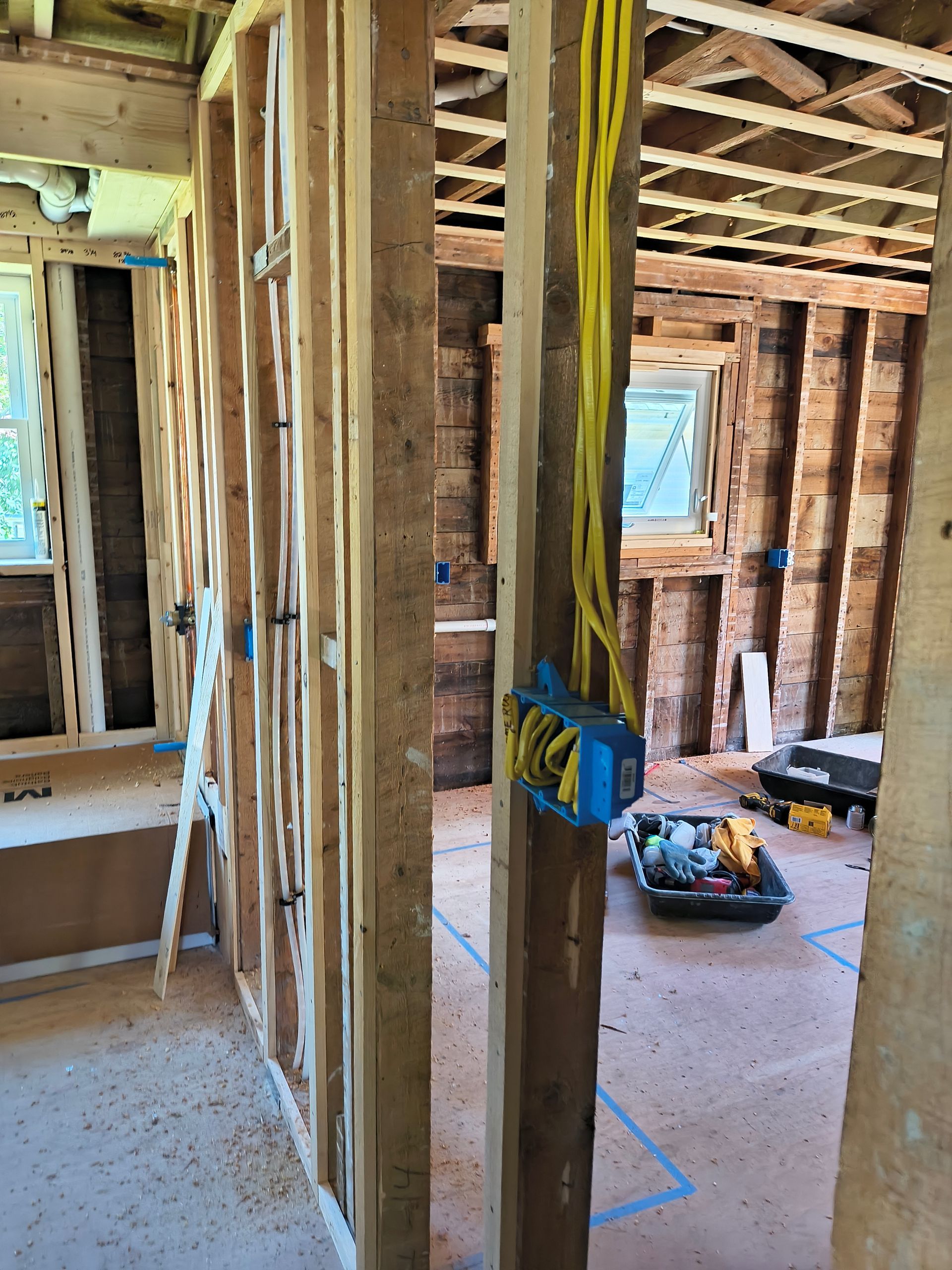 Interior view of a room under construction, showing wooden framing, electrical wiring, and blue electrical boxes.