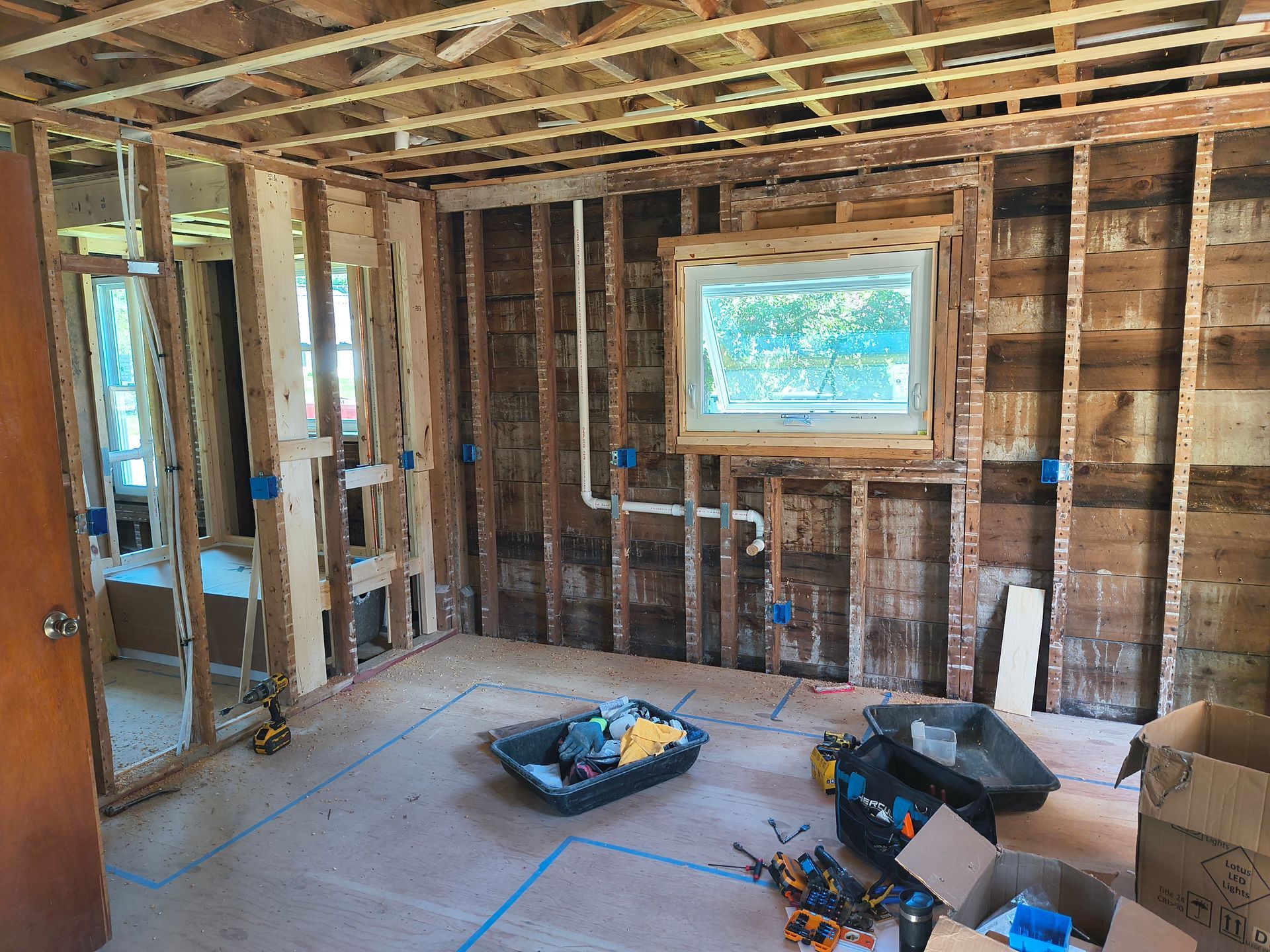 Room gutted for renovation, showing exposed wooden studs, wiring, and a window.