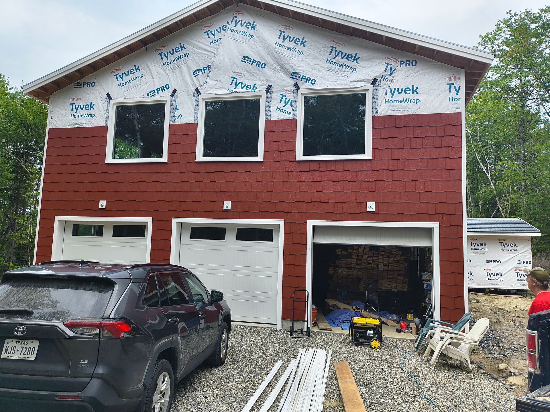 Two-story building under construction with red siding, white garage doors, and a car parked in front.