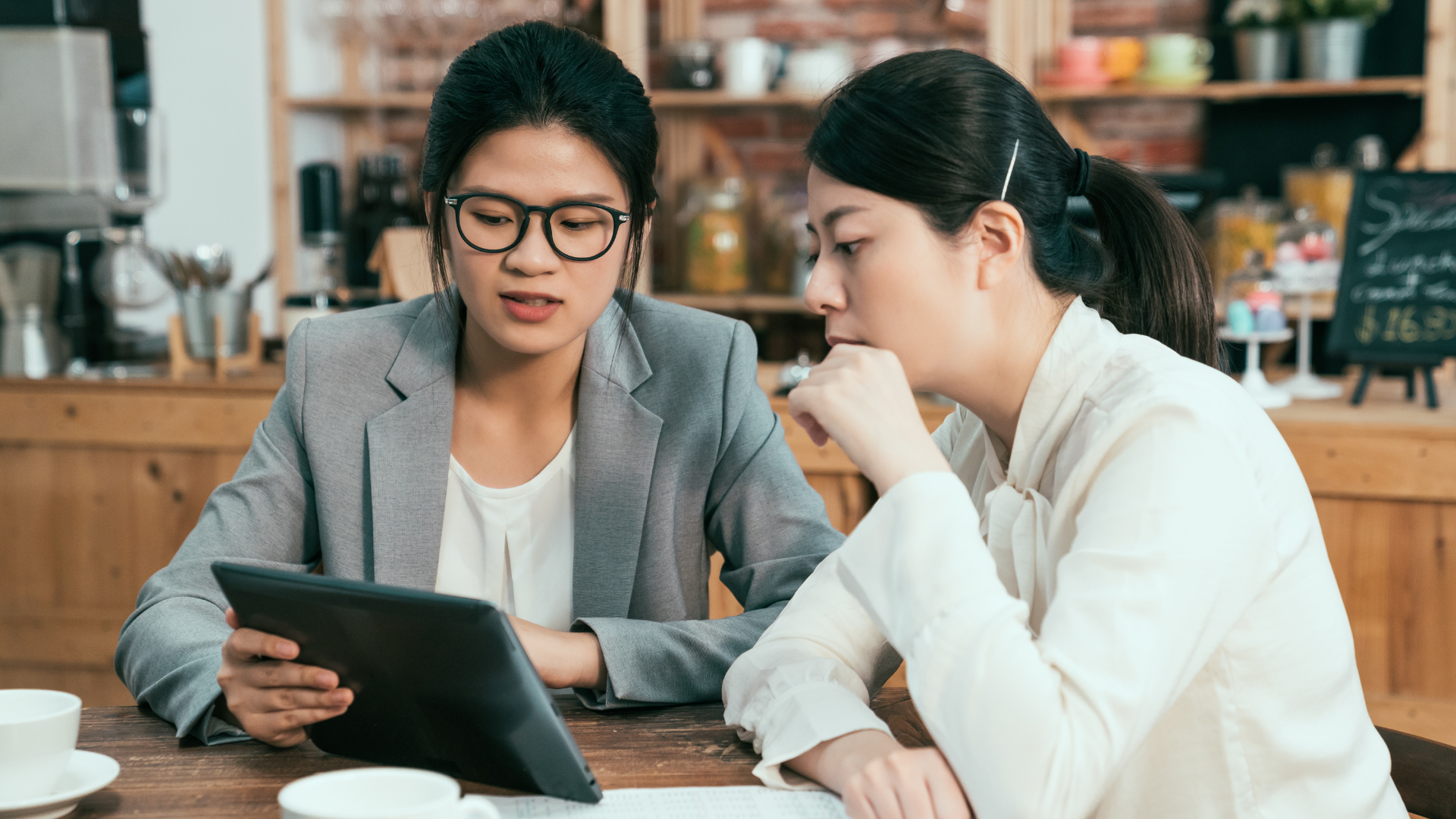 Two women are sitting at a table looking at a tablet.