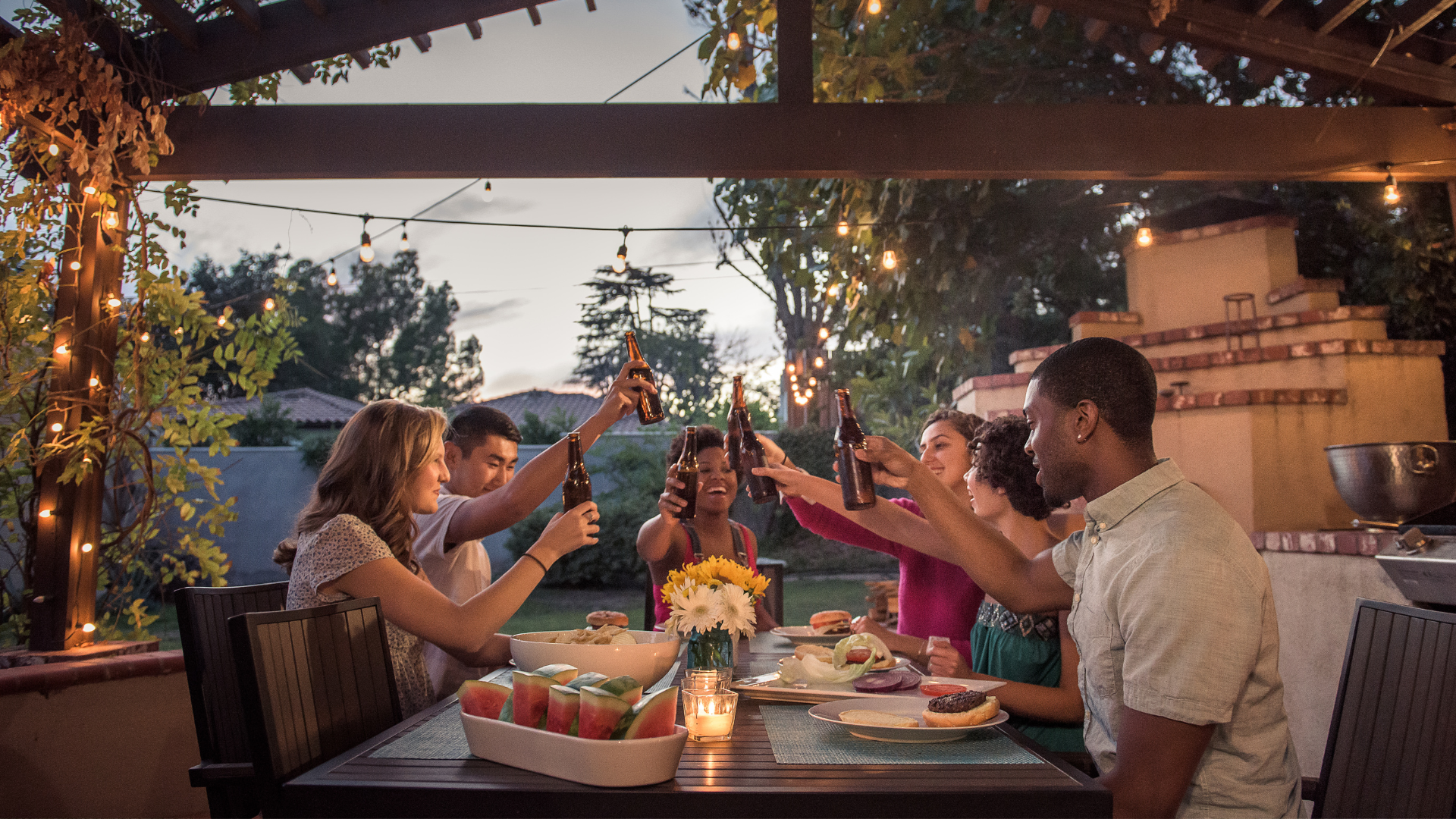 A group of people are sitting at a table toasting with beer bottles.