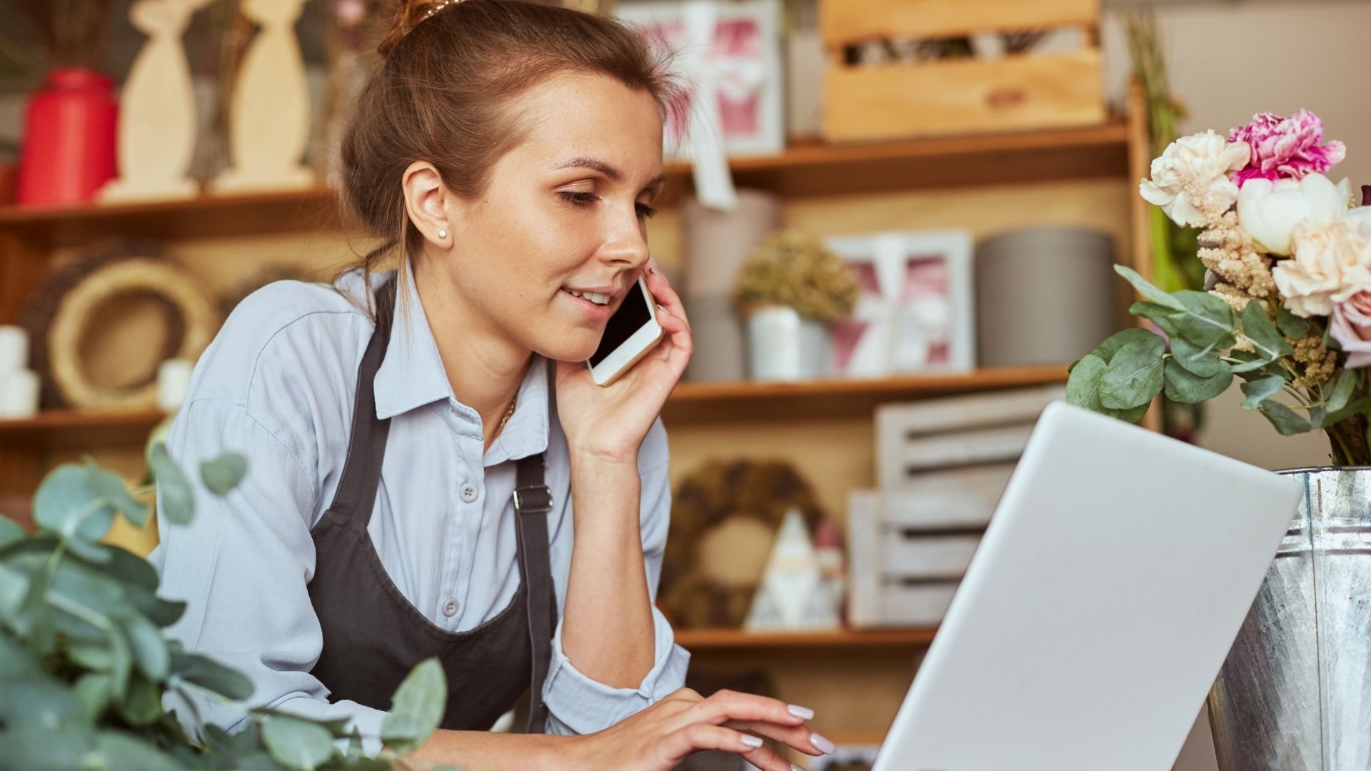 A woman is talking on a cell phone while using a laptop computer.
