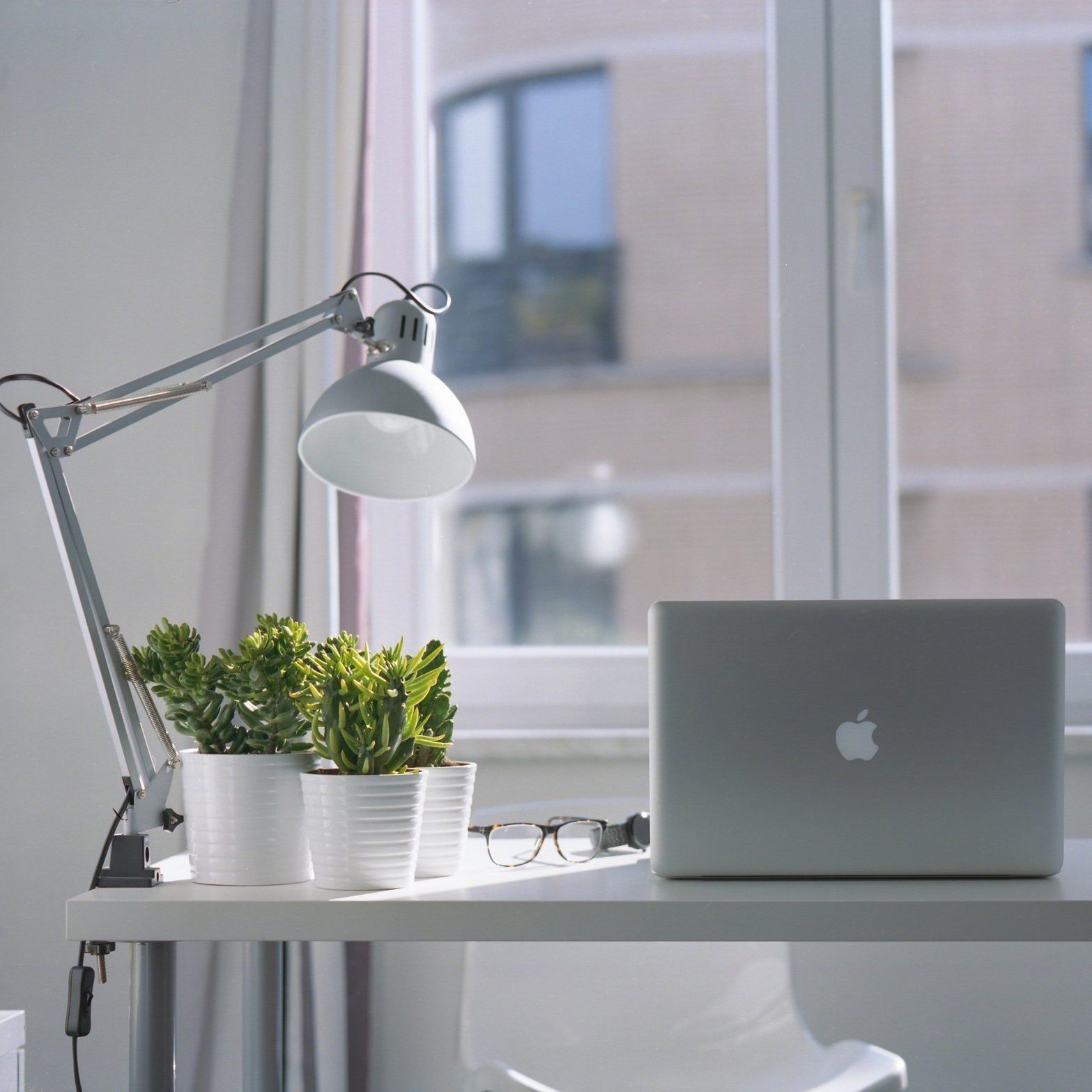 An apple laptop sits on a desk in front of a window