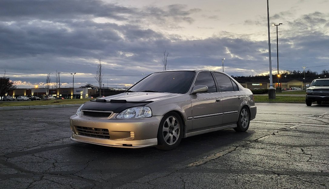 Tan Honda Civic parked on wet pavement under a cloudy sky.