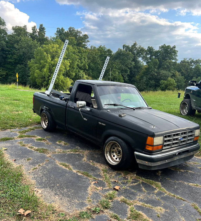 Black lowered Ford Ranger pickup truck parked on concrete, with two metal bars extending from the bed.