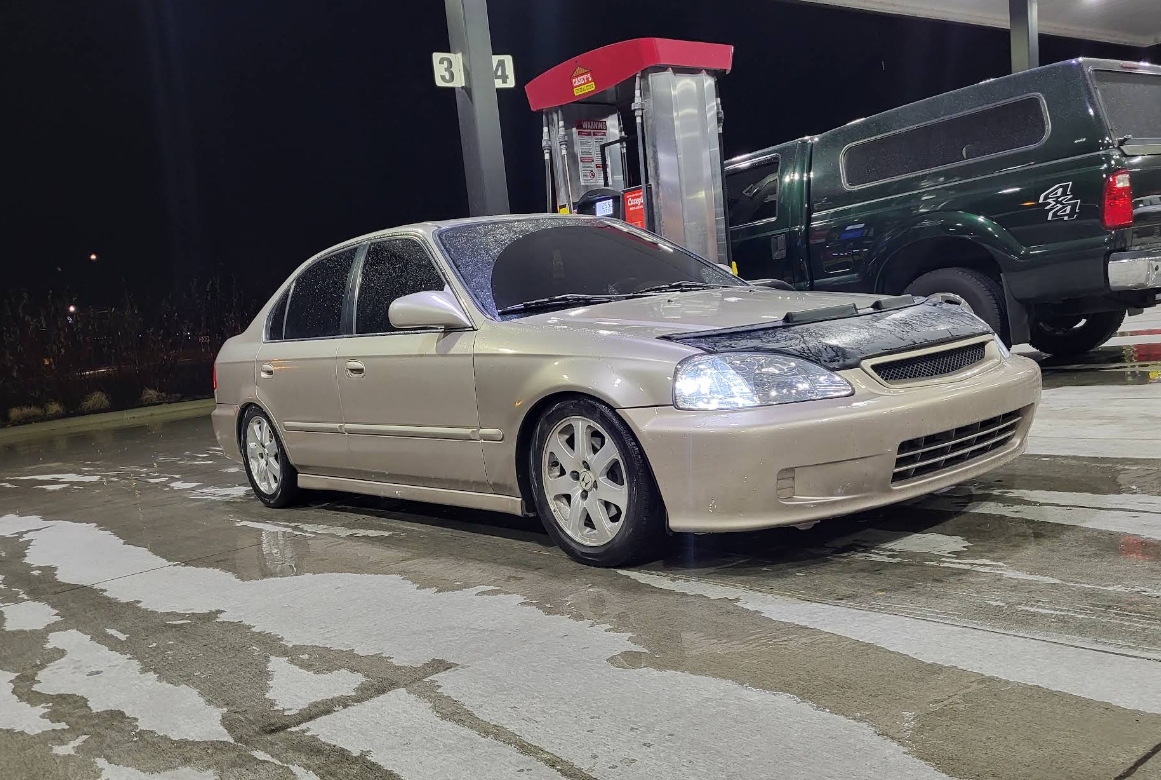 Gold Honda Civic at a gas station, nighttime. A black truck is in the background.