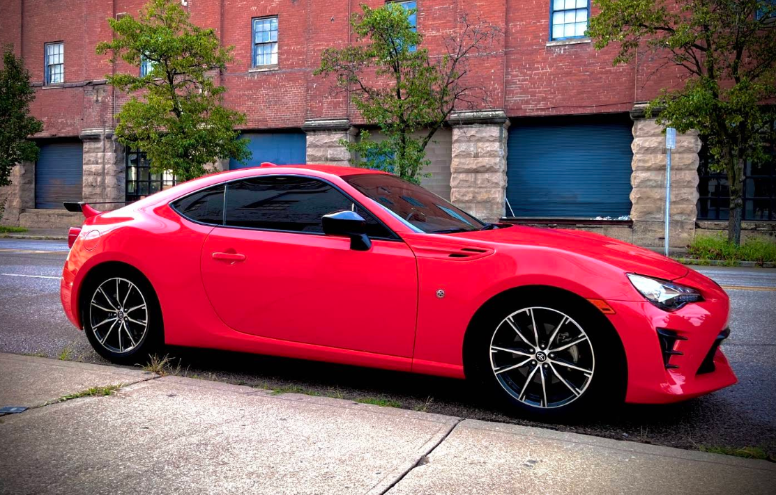Red sports car parked on a city street, in front of a red brick building.