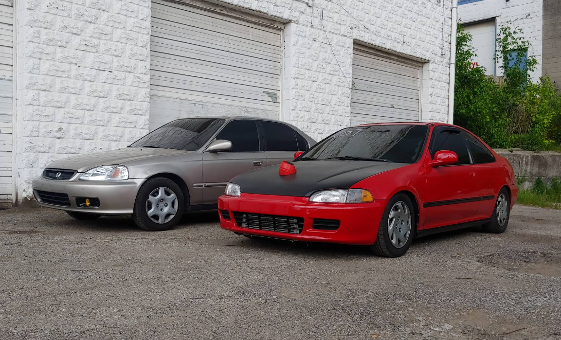 Two Honda Civics, silver and red, parked in front of a white brick building.