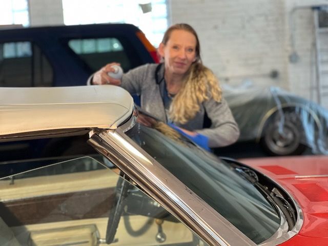 A woman is cleaning the windshield of a red car