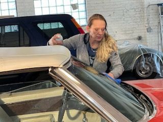 A woman is cleaning the windshield of a red car.
