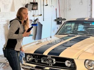 A woman is standing next to a mustang in a garage.