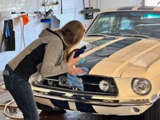 A woman is cleaning a mustang with a cloth in a garage.