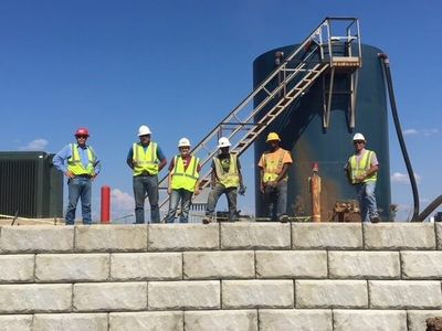 Construction crew wearing safety gear standing on top of a completed concrete block retaining wall at an industrial site during a concrete block retaining wall service in Herriman, UT