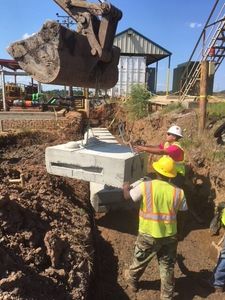 Large excavator lowering heavy concrete blocks into position while a worker guides placement during a concrete block retaining wall service in Herriman, UT
