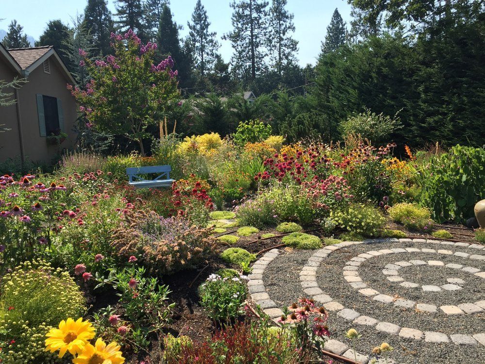 A colorful garden with a stone spiral path, flowers, and a small blue bench.