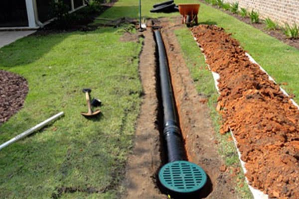 A trench with black drainage pipe and a green grate installed in a lawn.