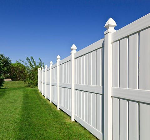 White vinyl fence on green grass against a clear blue sky.