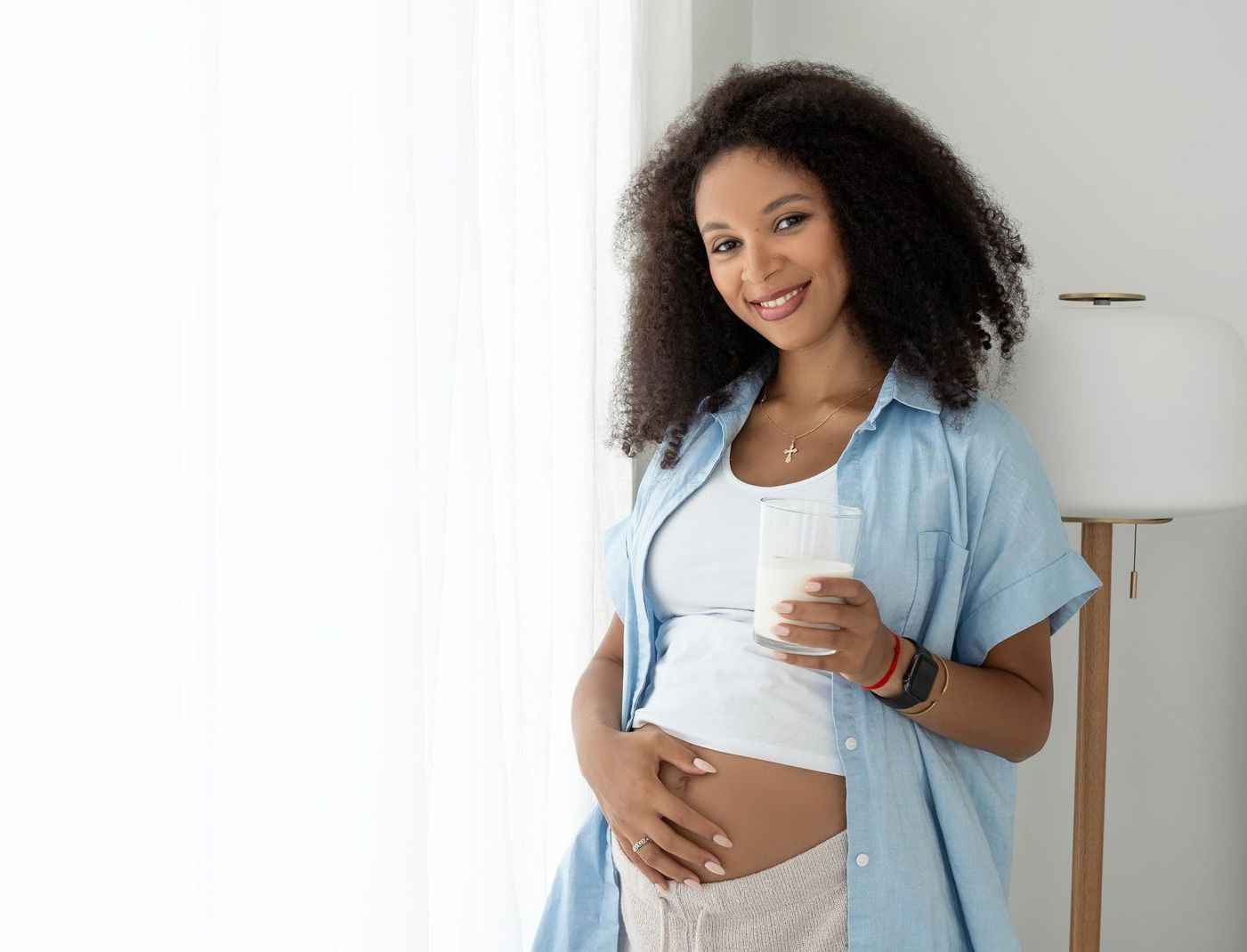 a pregnant woman is holding a glass of milk and smiling .